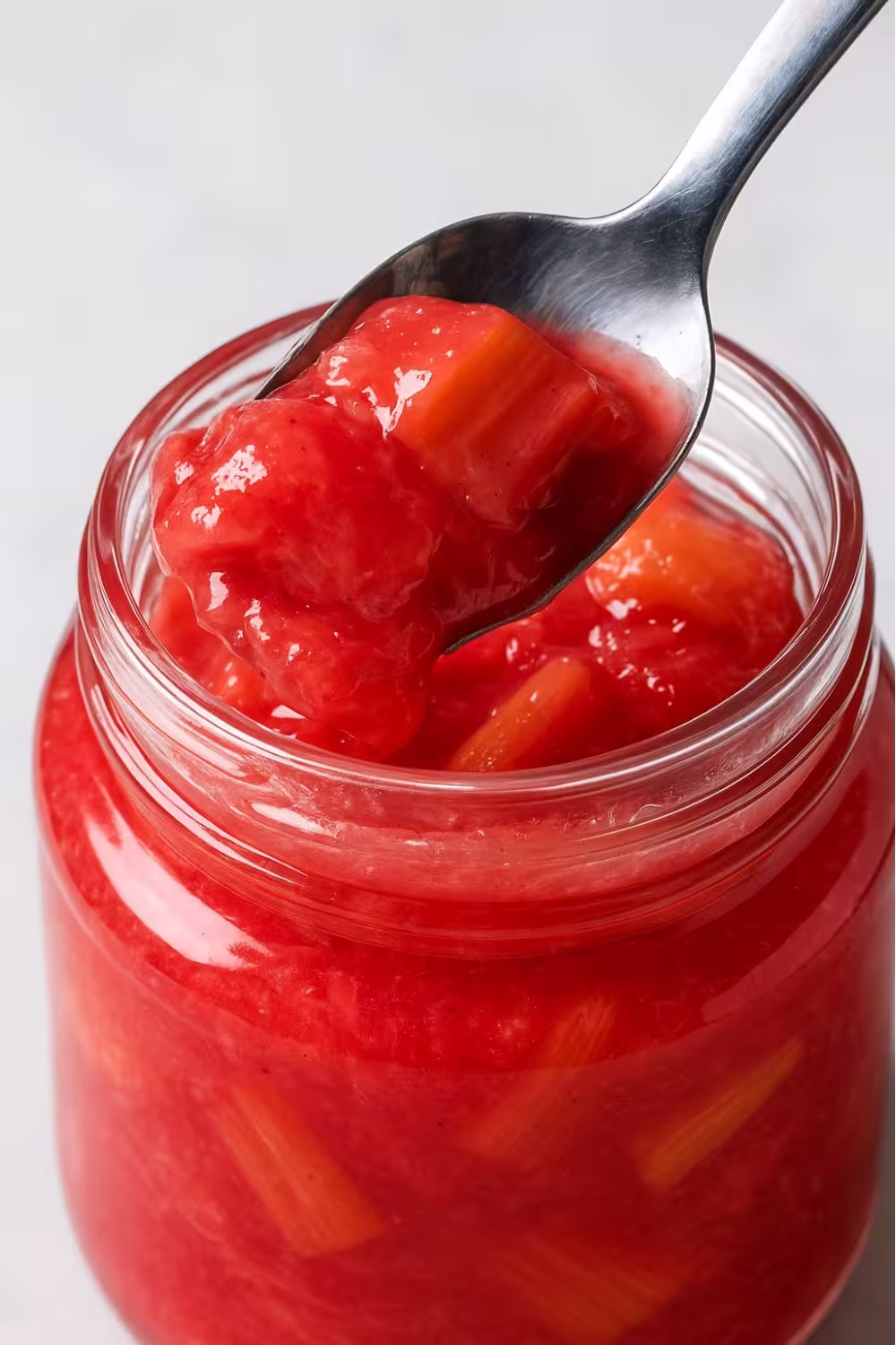 Spoonful of chunky rhubarb compote being lifted from a jar