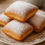 Fluffy vanilla French beignets dusted with powdered sugar on a vintage plate.