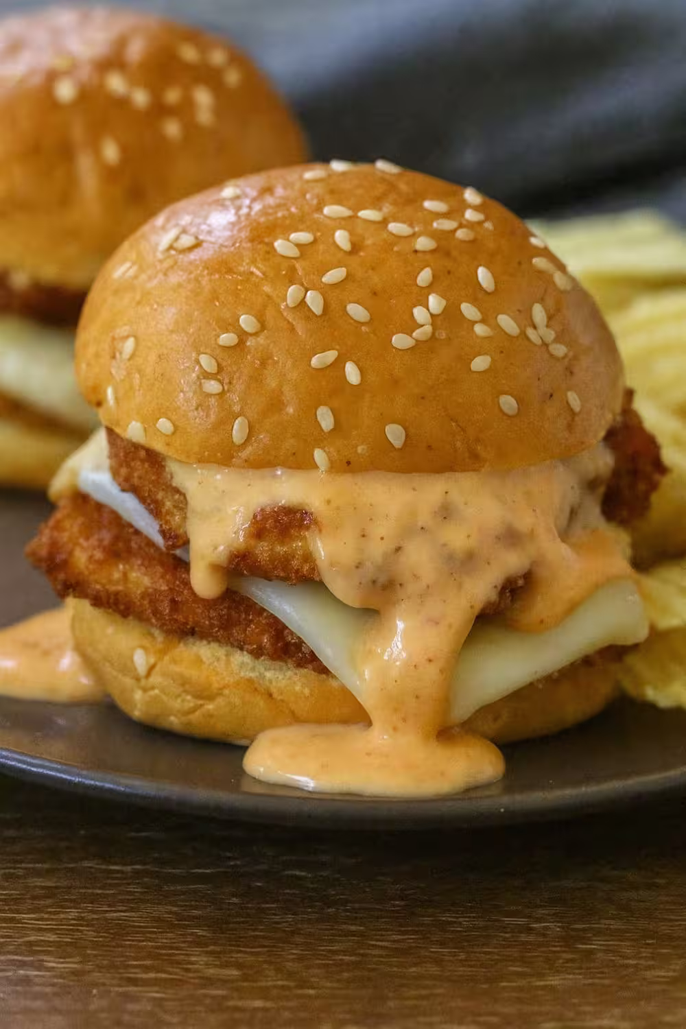 Close-up of a Bang Bang Chicken Slider with crispy chicken, melted cheese, and creamy sauce on a sesame seed bun.
