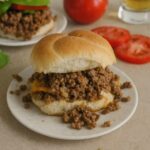 Crockpot cheeseburger with seasoned ground beef and melted cheese on a soft bun, served on a white plate.