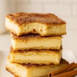 Stacked Churro Cheesecake Bars with a golden cinnamon-sugar crust, served on a white plate.