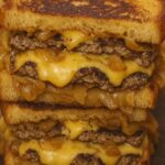 Close-up of a juicy patty melt with melted cheese, grilled onions, and toasted bread.