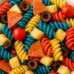 Patriotic red, white, and blue rotini pasta salad with olives, cheese, and pepperoni in a white bowl.