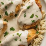 Creamy chicken breasts served over a bed of rice and garnished with fresh herbs.