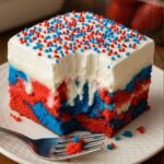 Red, white, and blue patriotic poke cake topped with whipped frosting and festive sprinkles.