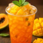 Chilled mango iced tea in a clear plastic cup topped with fresh mango cubes, mint leaves, and ice.