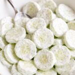 Sliced cucumbers coated in a creamy dill dressing, served in a white bowl.