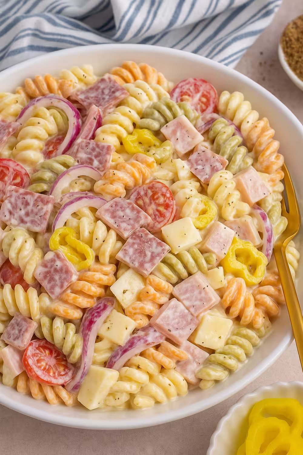 A colorful bowl of Grinder Pasta Salad with tri-color rotini, diced salami, cheese cubes, cherry tomatoes, red onions, and banana peppers, served with a creamy dressing.