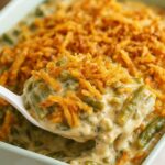 Creamy green bean casserole topped with crispy fried onions in a light green baking dish.