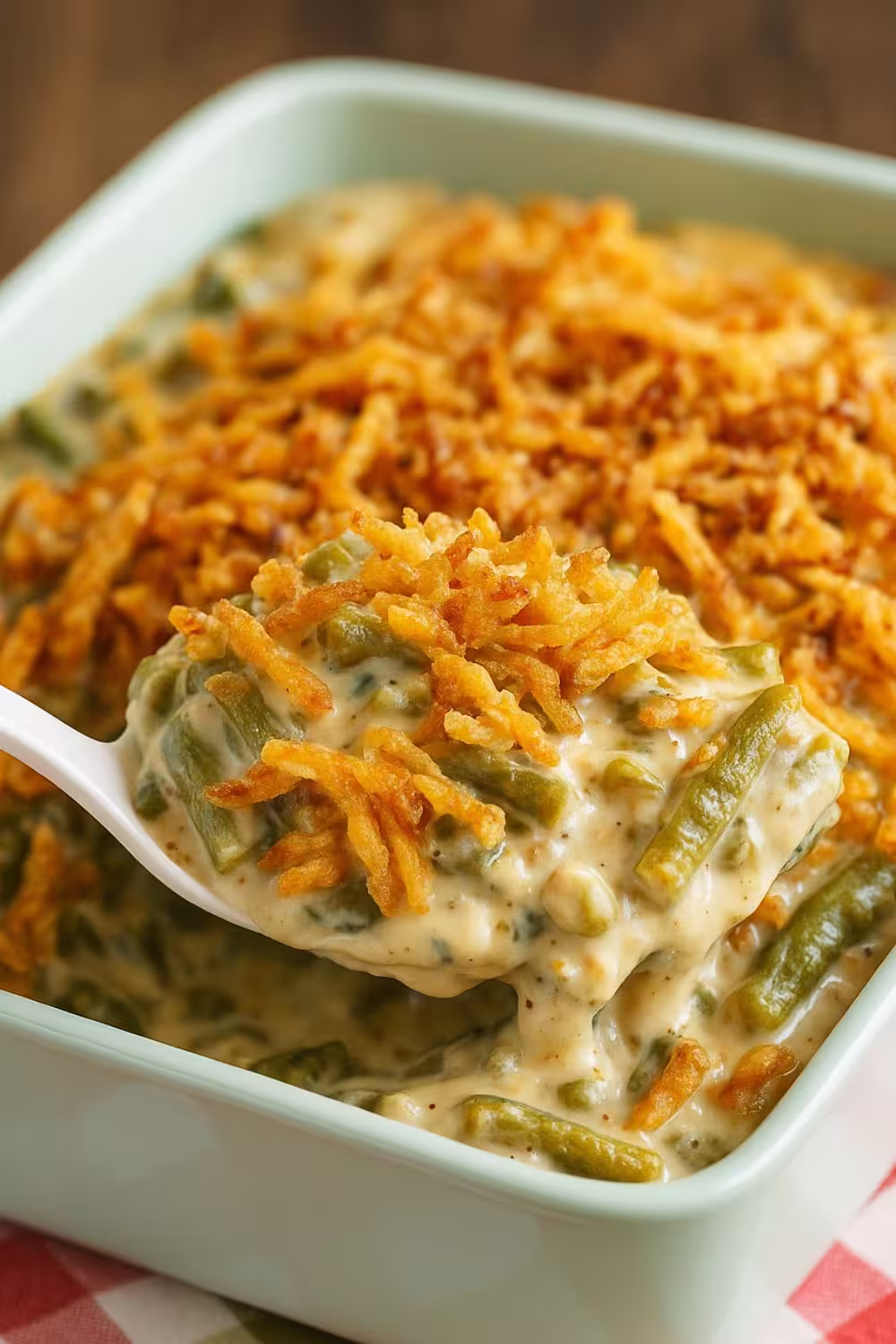 Creamy green bean casserole topped with crispy fried onions in a light green baking dish.