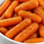 Glazed baby carrots coated in a glossy maple and brown sugar glaze in a white bowl.
