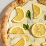 Freshly baked lemon pizza with melted cheese, parsley, and lemon slices on top.