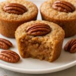 Mini pecan pie muffins with gooey centers, topped with whole pecans on a white plate