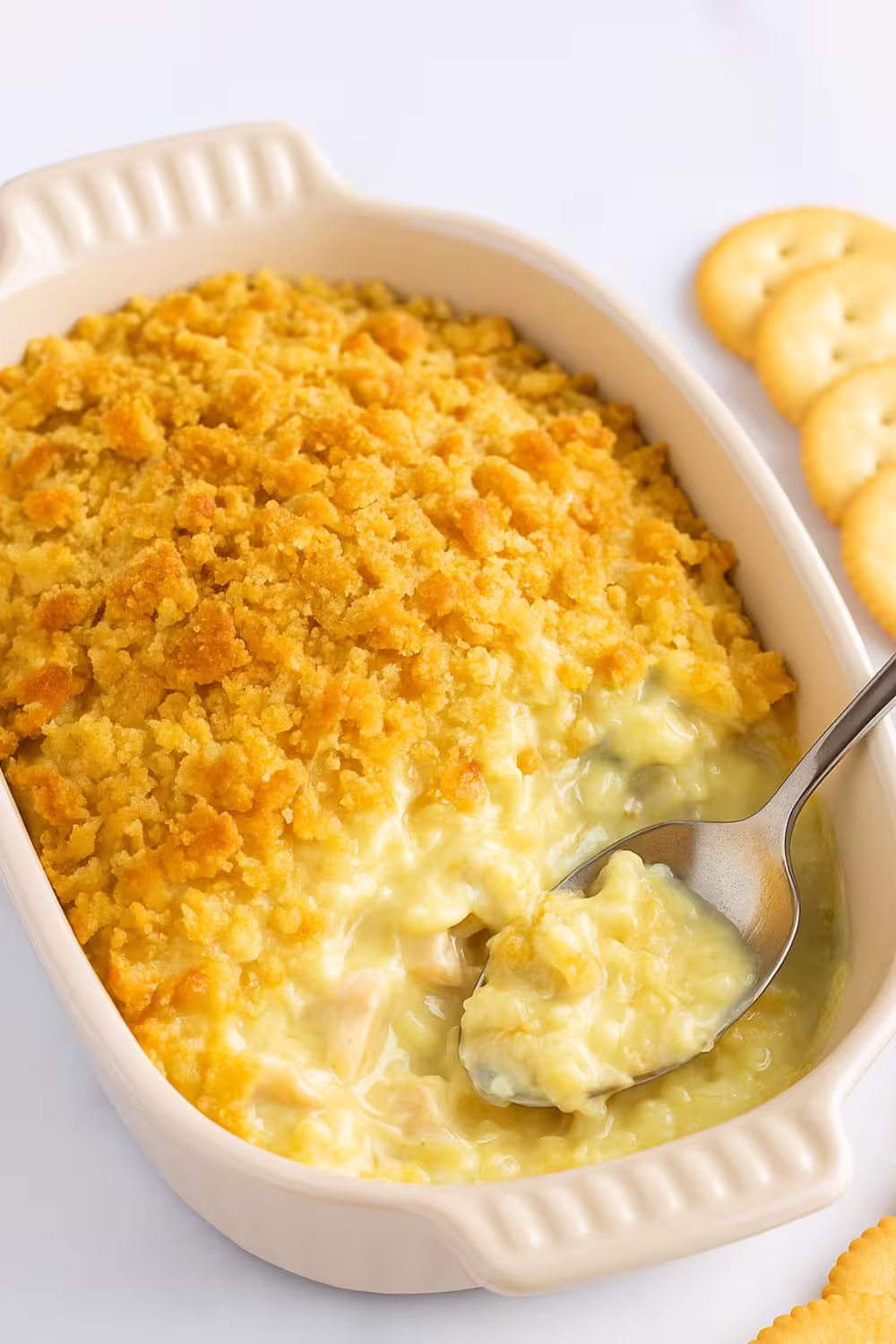 Creamy chicken Ritz casserole topped with golden buttery cracker crumbs in a baking dish with a spoon and Ritz crackers on the side.