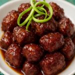 Close-up of crispy Chinese honey garlic chicken meatballs garnished with green onion curls in a white bowl.