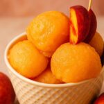 Creamy peach sorbet scoops served in a textured bowl, garnished with a fresh peach slice.