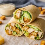 Three Chicken Caesar Wraps filled with crispy chicken, fresh lettuce, parmesan cheese, and creamy Caesar dressing, stacked on parchment paper.