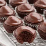 A batch of bite-sized Texas Sheet Cake Bites topped with smooth chocolate frosting, with one showing a bite taken out to reveal the moist interior.
