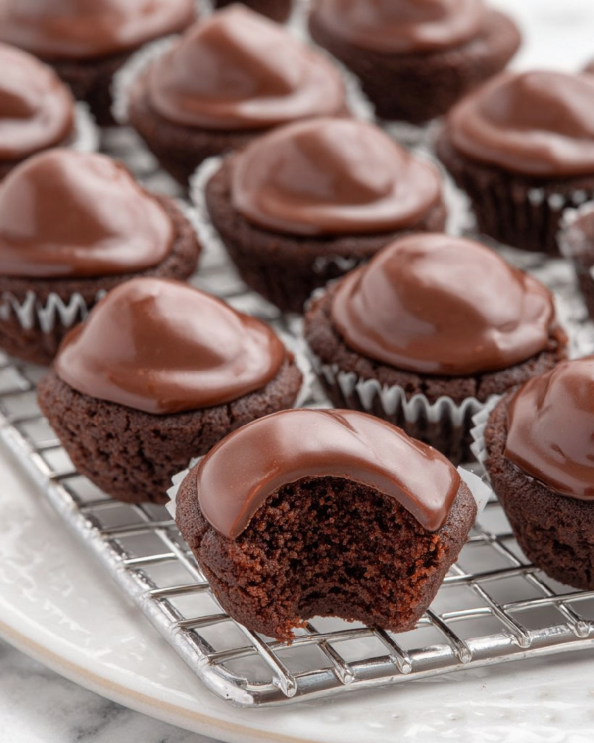 A batch of bite-sized Texas Sheet Cake Bites topped with smooth chocolate frosting, with one showing a bite taken out to reveal the moist interior.
