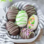 A basket filled with chocolate-covered and white-coated peanut butter eggs decorated with colorful sprinkles and drizzle.