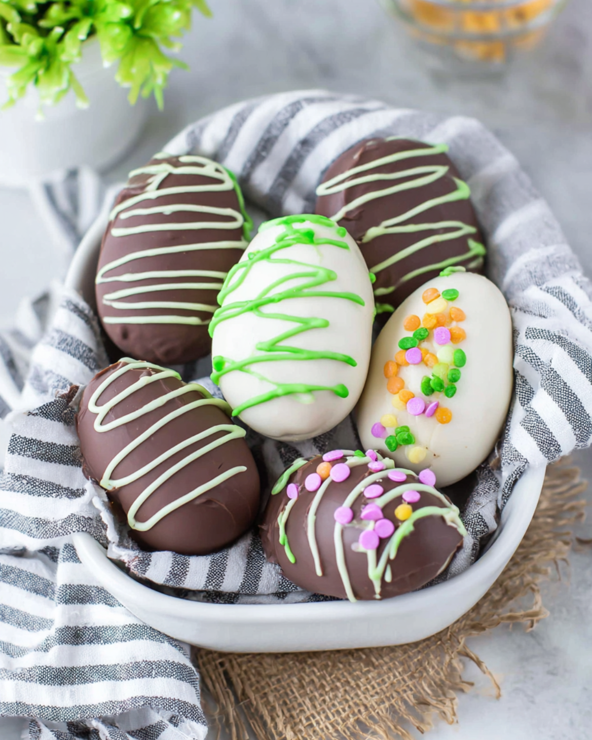 A basket filled with chocolate-covered and white-coated peanut butter eggs decorated with colorful sprinkles and drizzle.