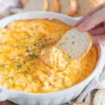 Bahama Breeze crab dip recipe served hot in a white baking dish, with melted cheese on top and sliced bread for dipping.