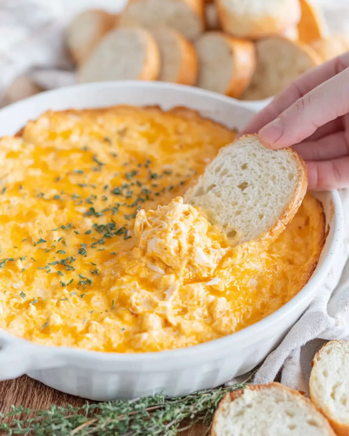 Bahama Breeze crab dip recipe served hot in a white baking dish, with melted cheese on top and sliced bread for dipping.