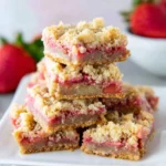 Keto Rhubarb Dream Bars stacked on a white plate, featuring a golden crumb topping and a pink rhubarb filling.
