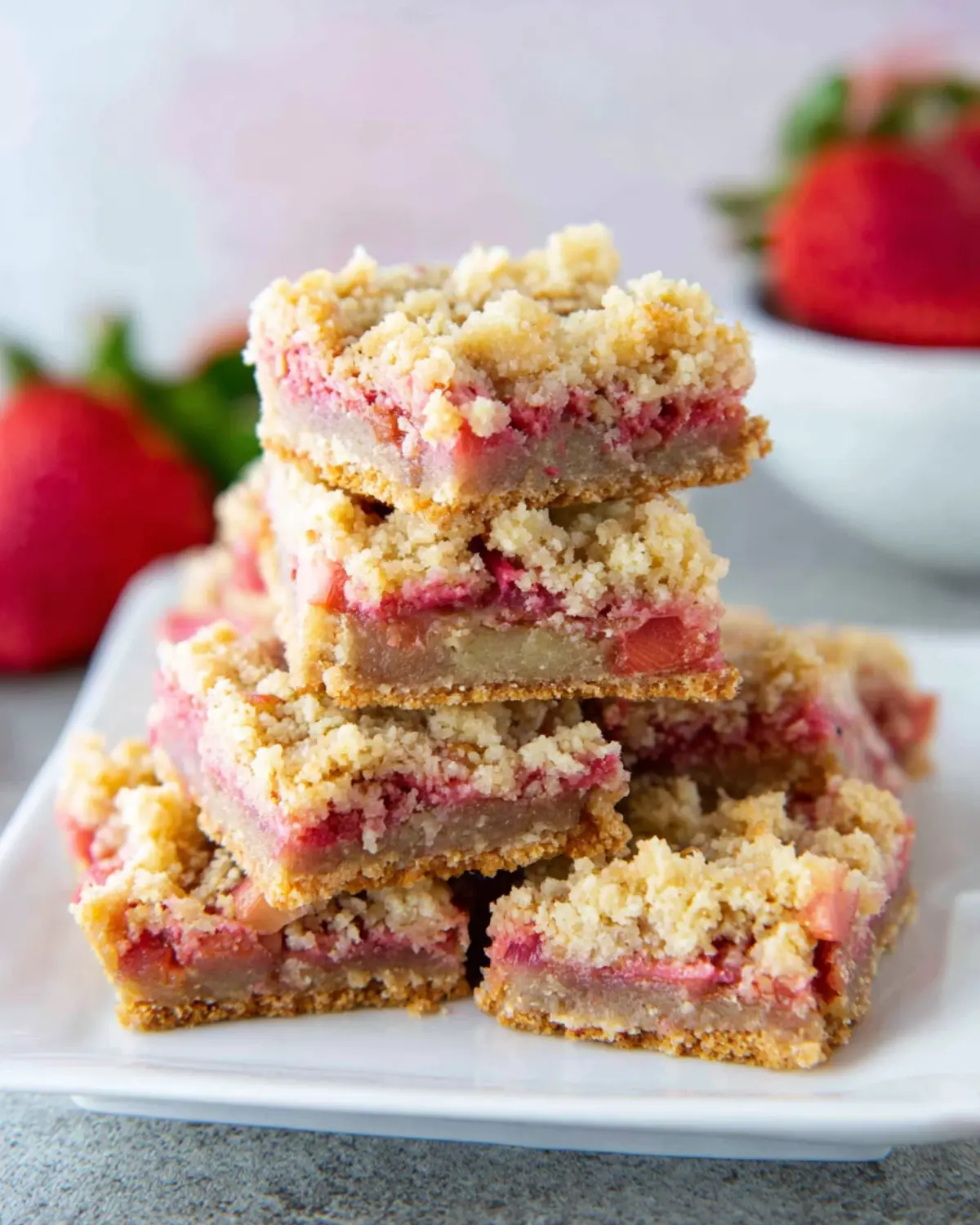Keto Rhubarb Dream Bars stacked on a white plate, featuring a golden crumb topping and a pink rhubarb filling.