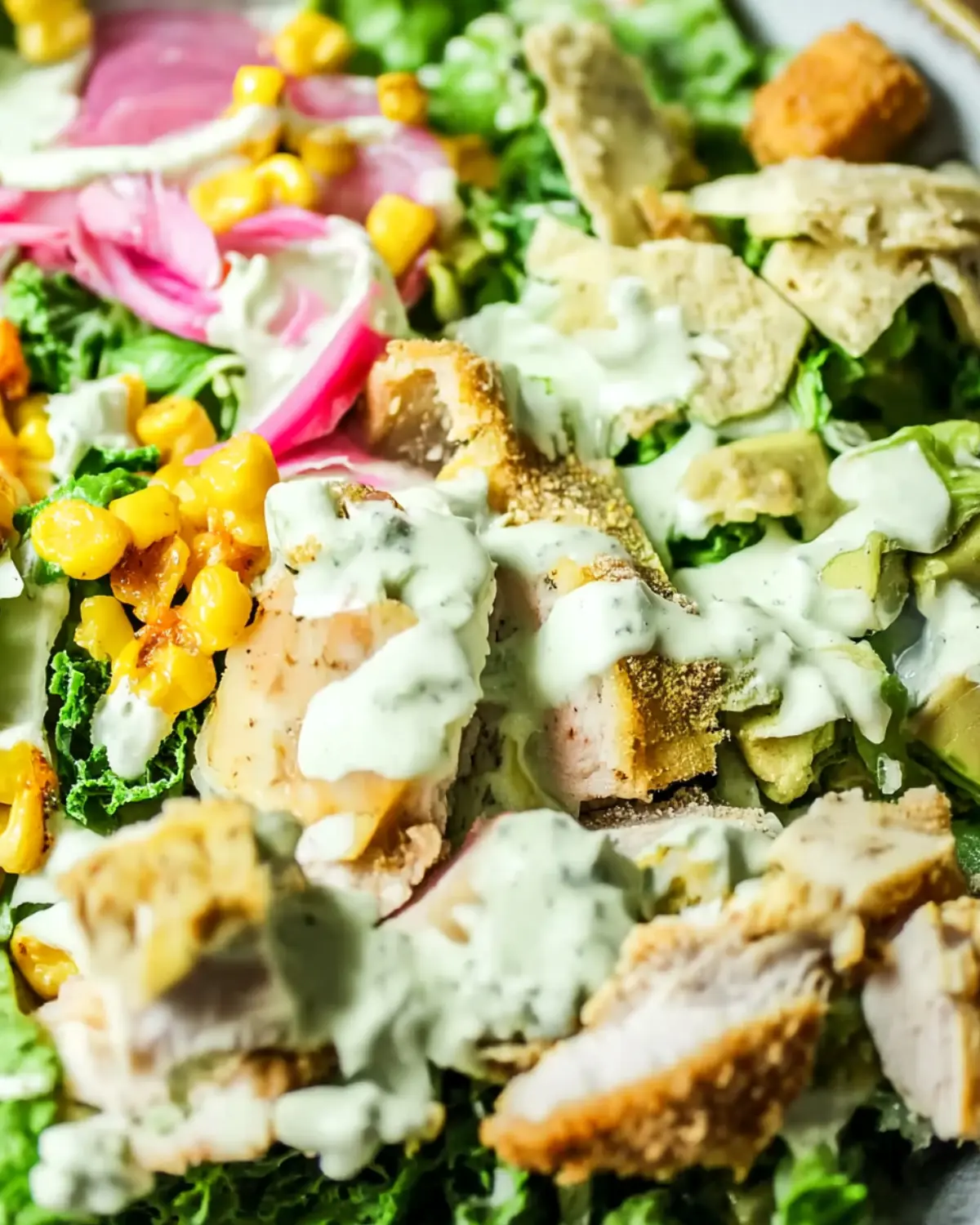 Close-up of a crispy chicken poblano salad topped with creamy dressing, corn, pickled onions, and greens.