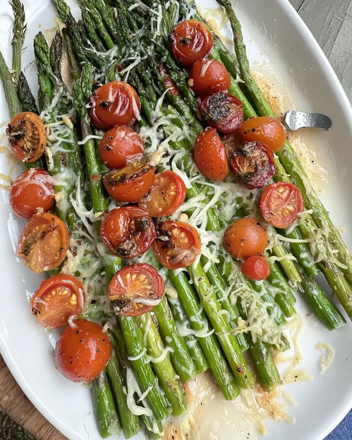 Roasted asparagus with cherry tomatoes and melted parmesan on a white serving dish.