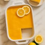 Bright yellow Limoncello Tiramisu bars with fresh lemon slices on top in a white baking dish.