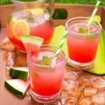 Two glasses of Watermelon Lemonade garnished with mint and watermelon slices, served on a wooden tray with a pitcher in the background.