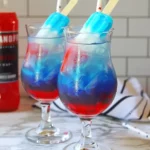 Two vibrant Bomb Pop Cocktails layered in red, blue, and white with a blue popsicle garnish in each glass.