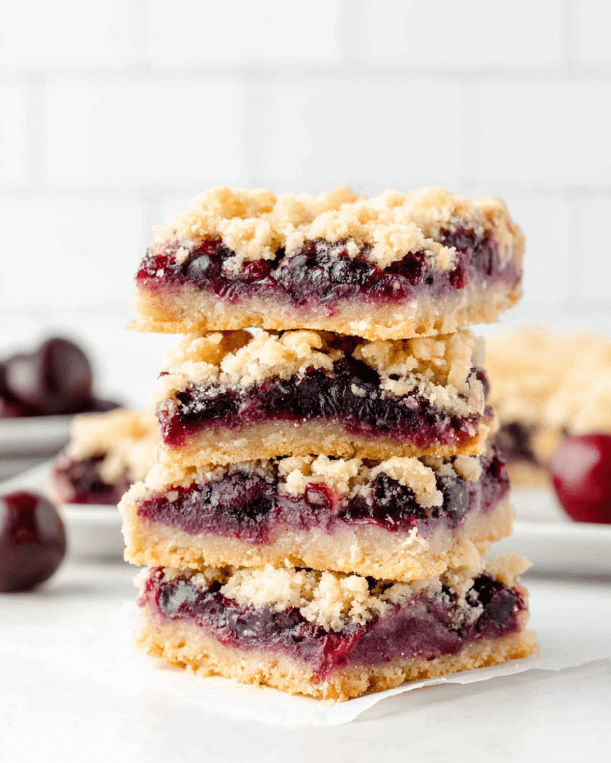 A stack of sour cherry crumble bars with buttery crust, juicy cherry filling, and crumbly topping on a white surface.