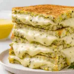 Stack of zucchini grilled cheese sandwiches with melted cheese oozing out on a white plate.