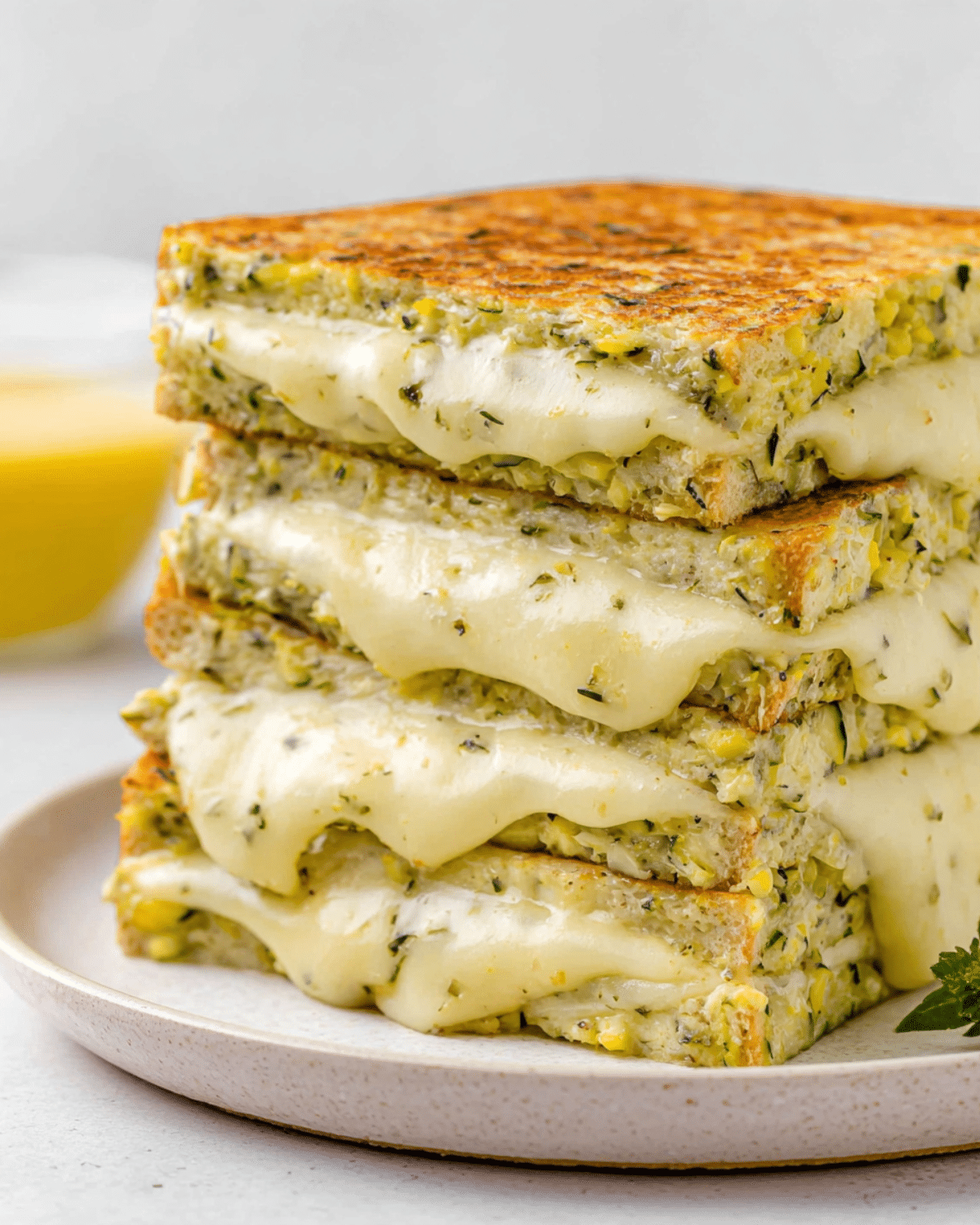 Stack of zucchini grilled cheese sandwiches with melted cheese oozing out on a white plate.