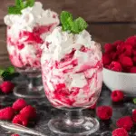 Glasses filled with easy raspberry eton mess made with whipped cream, raspberry sauce, and meringue, garnished with mint.