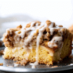 Close-up of a slice of apple crumb cake topped with cinnamon crumble and vanilla glaze.