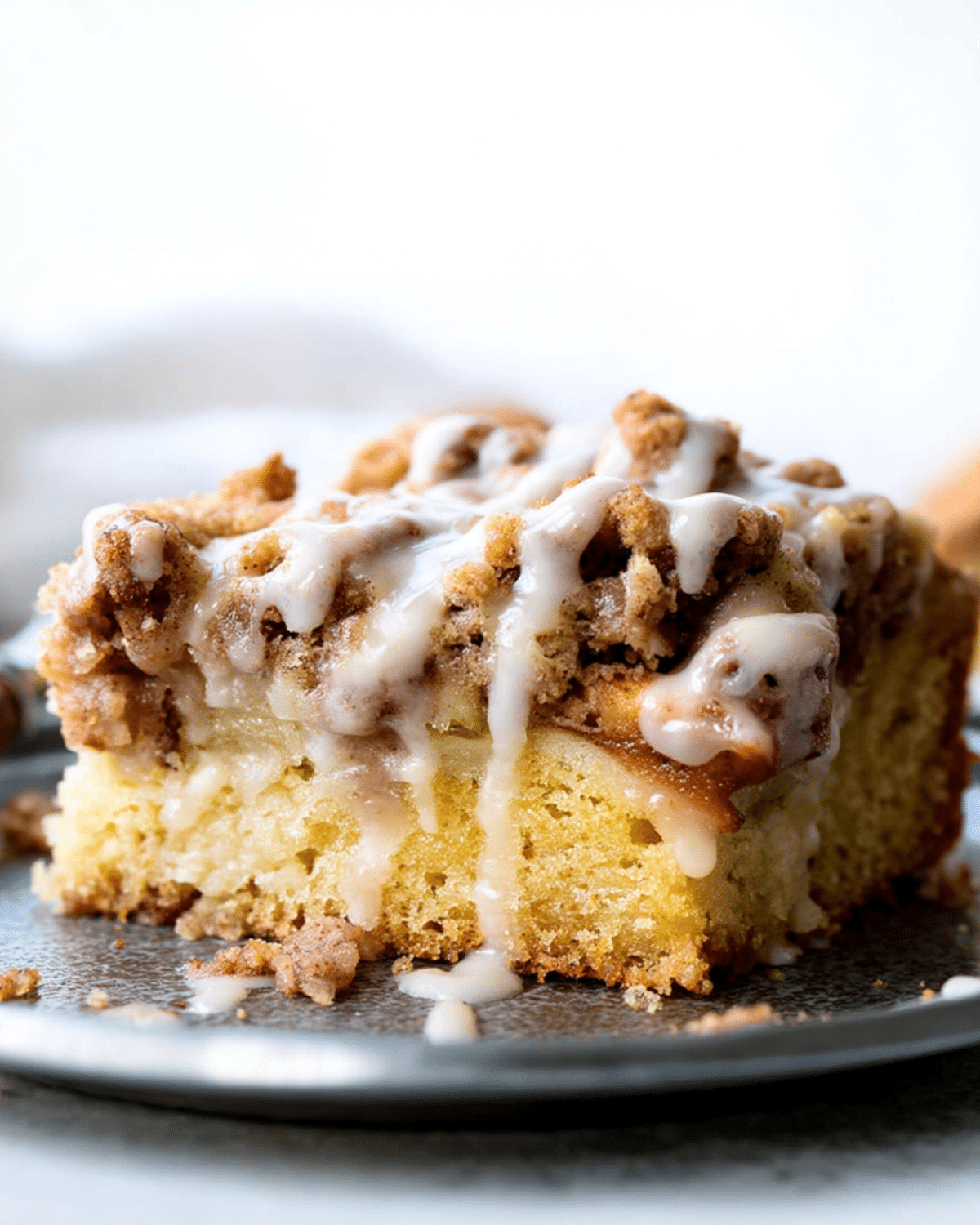 Close-up of a slice of apple crumb cake topped with cinnamon crumble and vanilla glaze.
