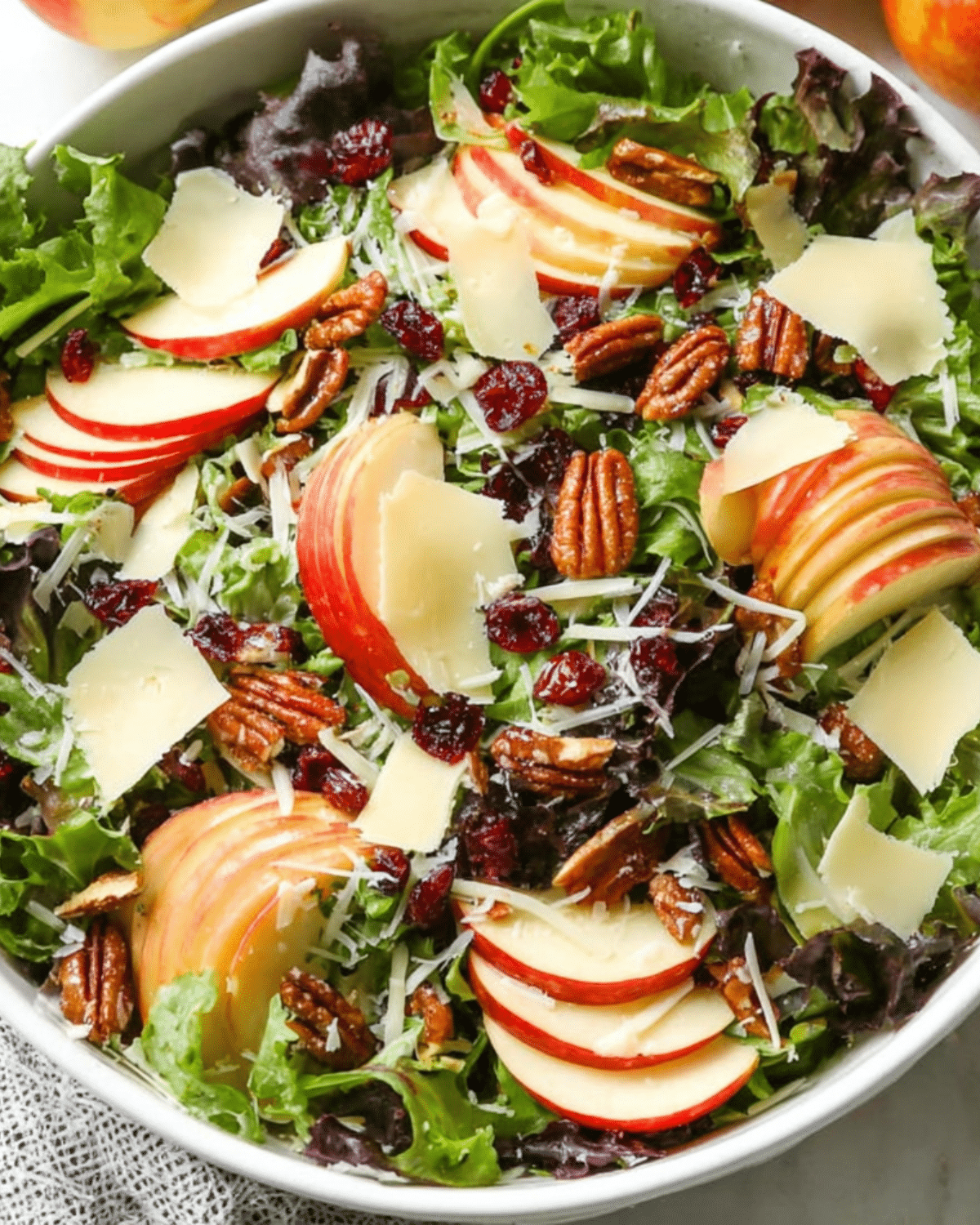 Apple Salad with Cheddar featuring fresh greens, sliced apples, cheddar cheese, pecans, and dried cranberries in a white bowl.