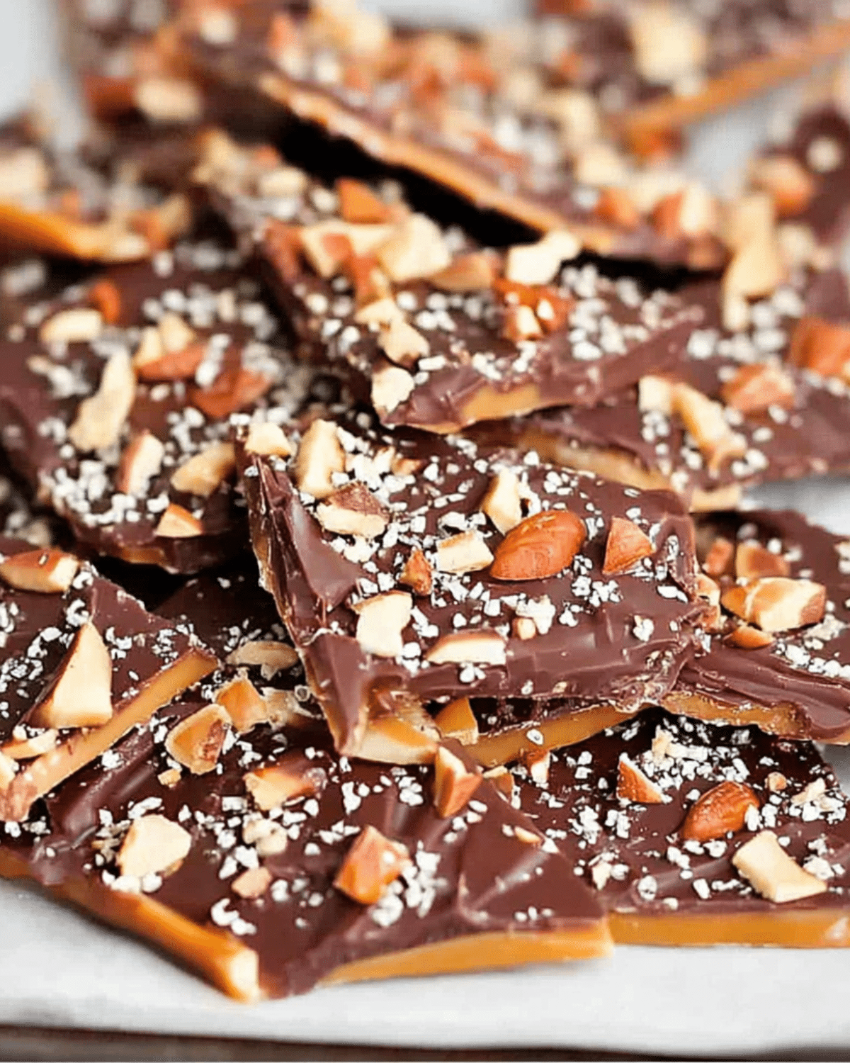 Close-up of Better Than Anything Toffee pieces topped with chopped almonds and sea salt on a parchment-lined tray.