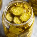 Jar of bread and butter pickles with cucumber slices in a tangy brine mixed with spices and red pepper flakes.