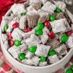 Bowl of Christmas Puppy Chow with powdered sugar, red and green candies, and chocolate-coated cereal.