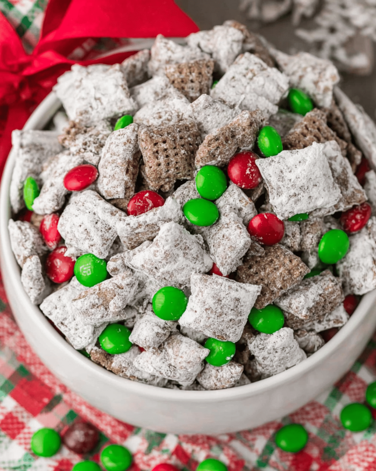 Bowl of Christmas Puppy Chow with powdered sugar, red and green candies, and chocolate-coated cereal.