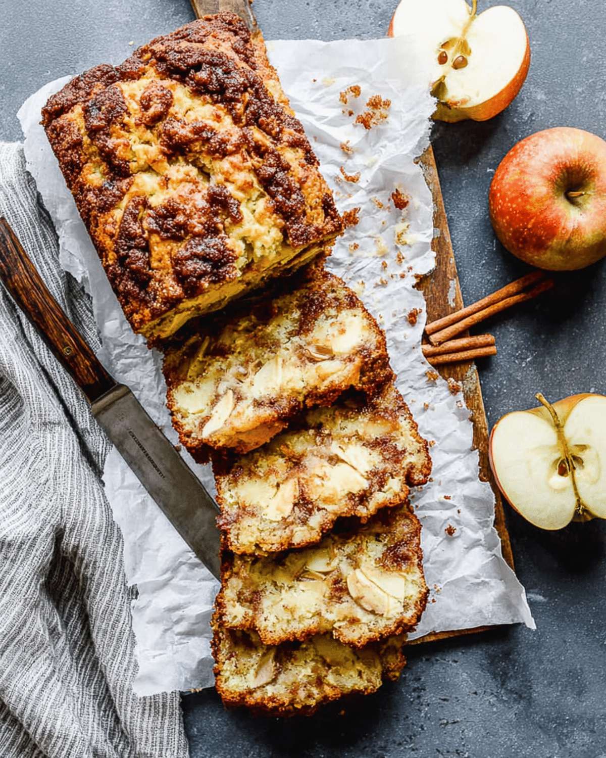 Cinnamon Apple Bread loaf with slices showing apple chunks and cinnamon swirl, served on parchment with fresh apples.