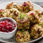 Cranberry Turkey Stuffing Balls served on a plate with fresh herbs and a side of cranberry sauce.