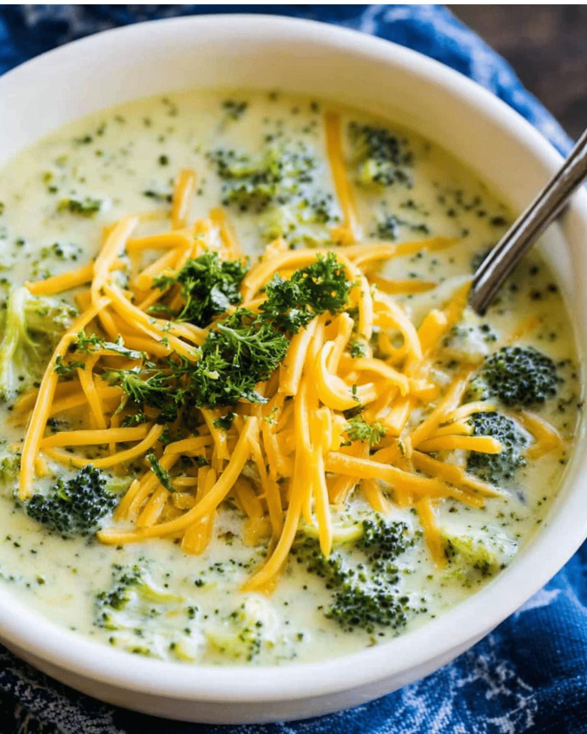 A bowl of creamy broccoli cheese soup topped with shredded cheddar cheese and fresh parsley.