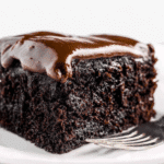 A slice of rich and moist chocolate Depression cake topped with glossy chocolate frosting on a white plate.