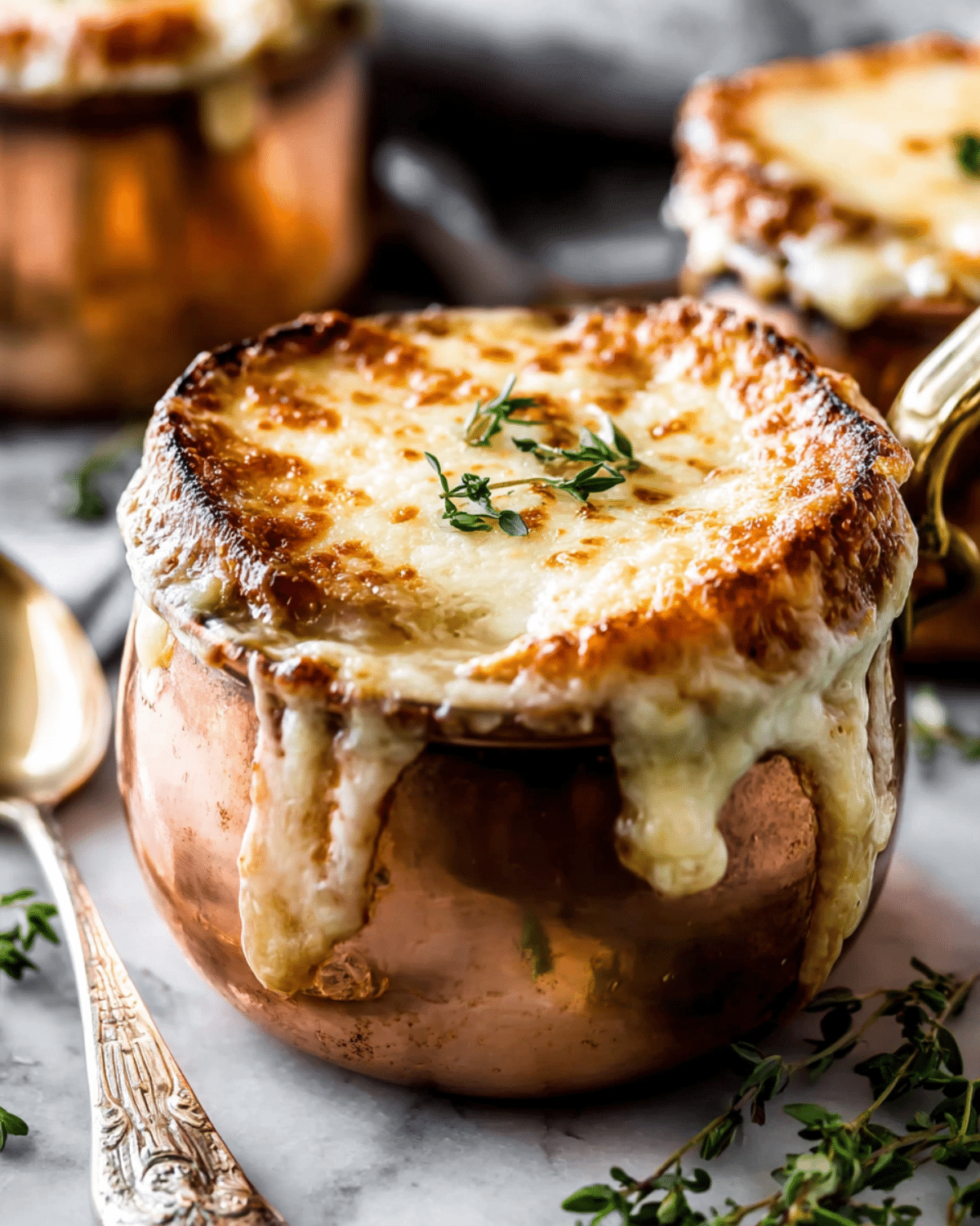 Copper pot of easy French onion soup topped with golden, melted cheese and garnished with fresh thyme.